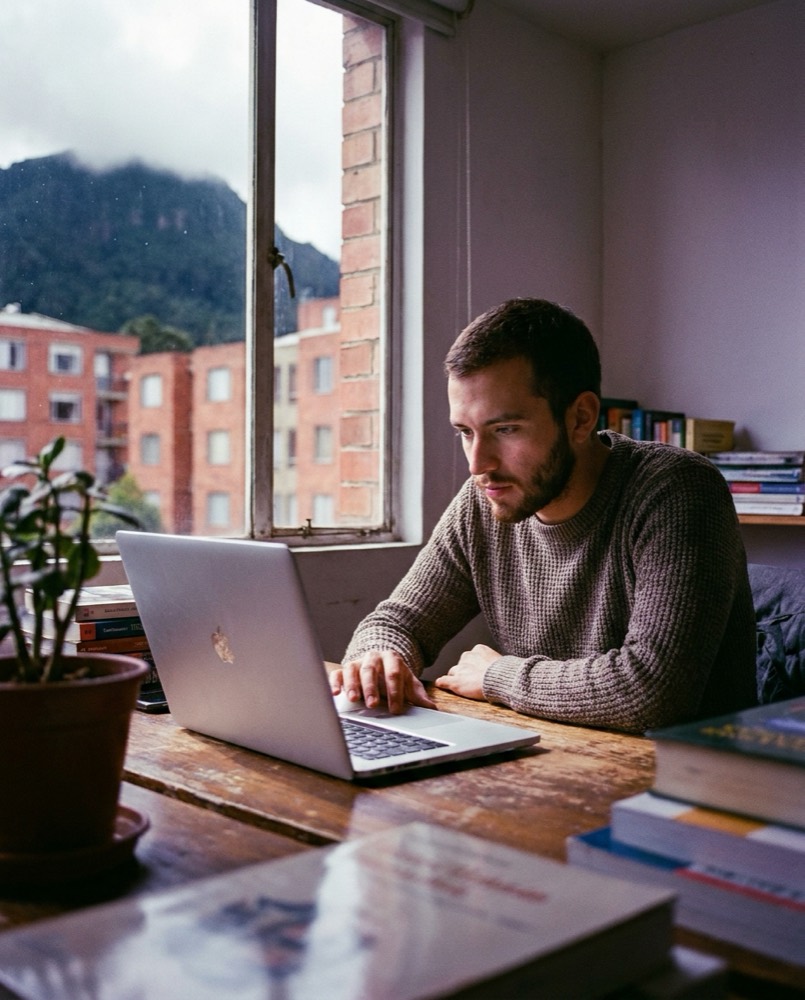 Estudiante rindiendo un examen en línea en su laptop, en Bogotá, con el cerro de Monserrate por la ventana