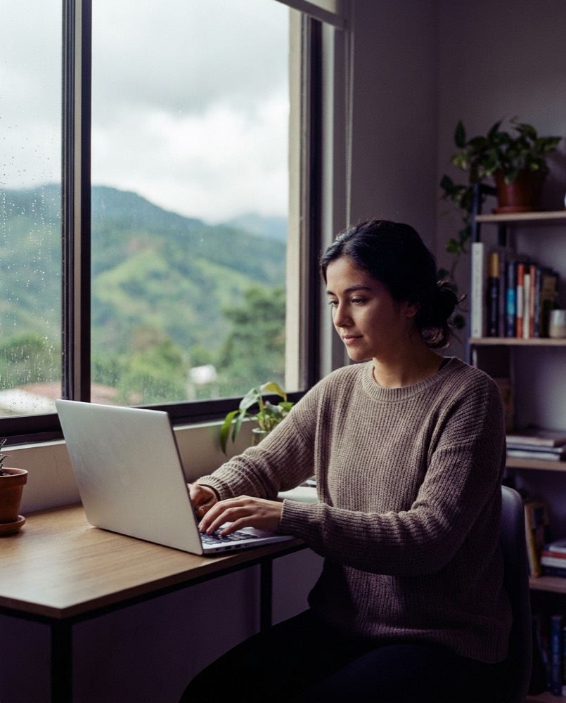 Estudiante rindiendo un examen en línea en su laptop, en San José, con montañas verdes del Valle Central por la ventana