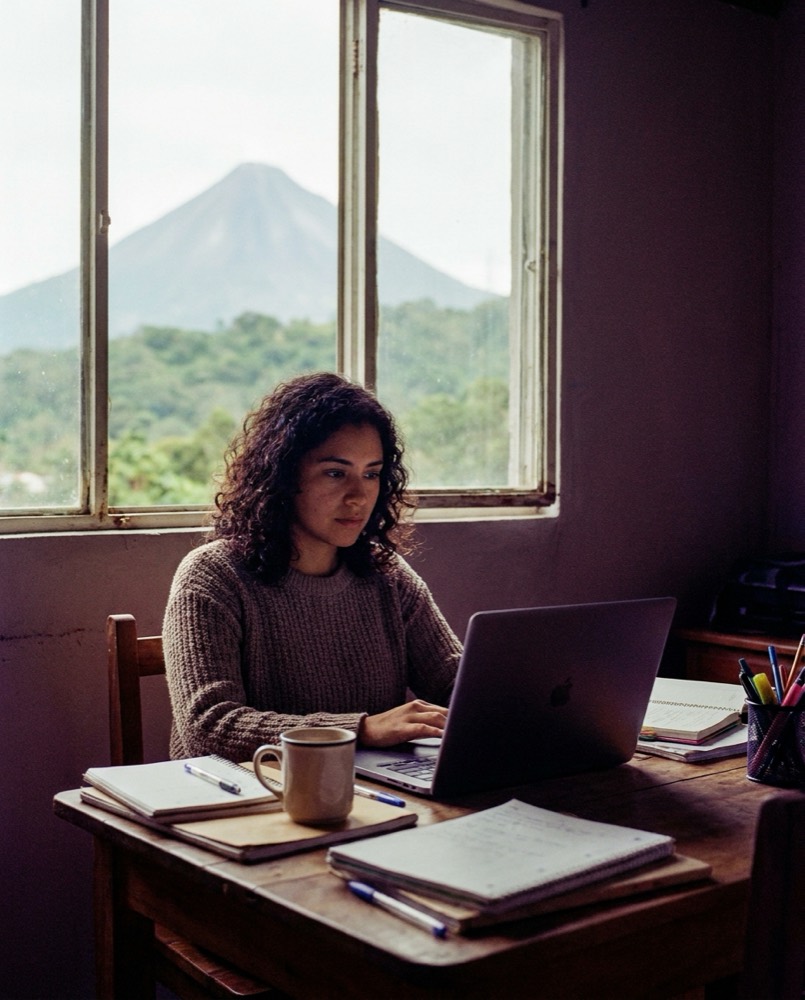 Estudiante rindiendo un examen en línea en su laptop, en Guatemala, con el volcán de Agua por la ventana