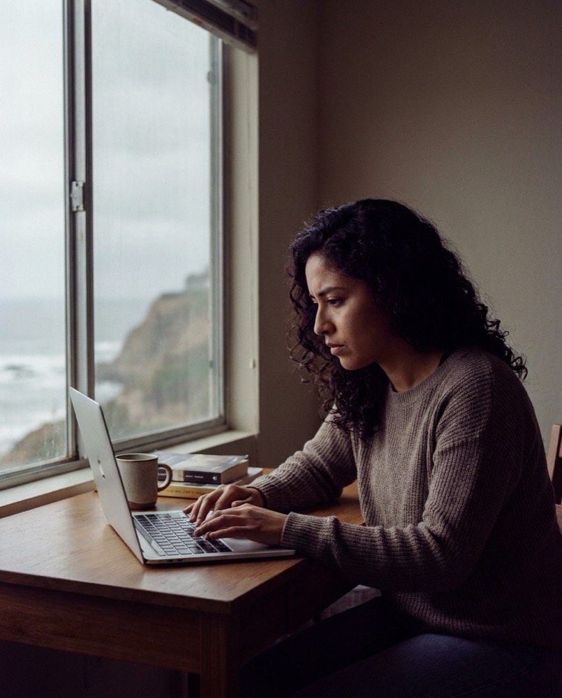 Estudiante rindiendo un examen en línea en su laptop, en un departamento de Lima con vista al mar
